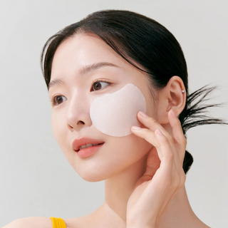 Woman applying a patch to her face against a plain background