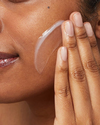 Close-up of a woman applying a skincare product to her cheek.