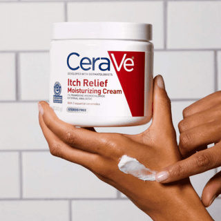 CeraVe Itch Relief Moisturizing Cream jar held by a hand with cream on the palm against a tiled wall background
