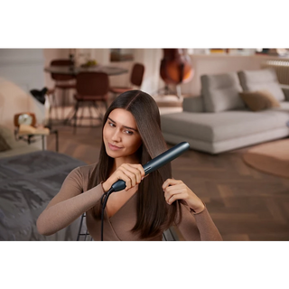 Woman using a hair straightener in a living room setting