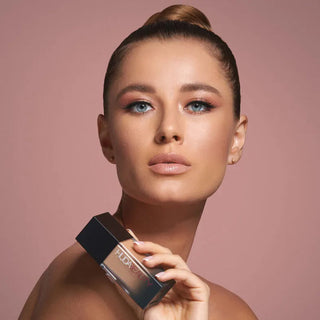 Woman holding a makeup product against a pink background