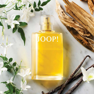 JOOP! perfume bottle with vanilla beans and flowers on a light background