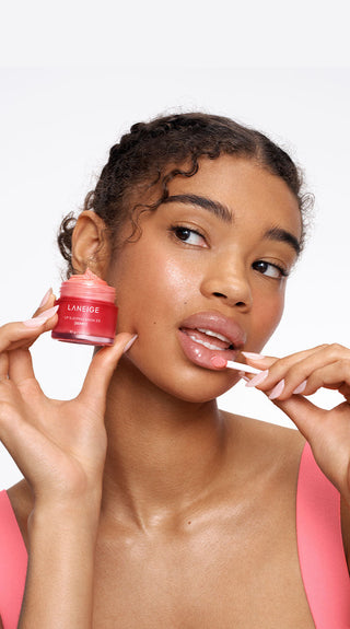 Woman applying a pink cosmetic product to her lips with a white background