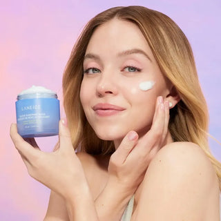 Woman applying Laneige product to her face with a pink and purple gradient background