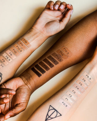 Two arms with brown makeup swatches on a beige background