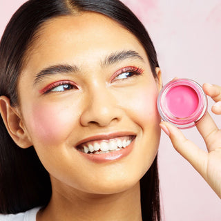 Woman applying pink blush to her cheek with a pink makeup container.