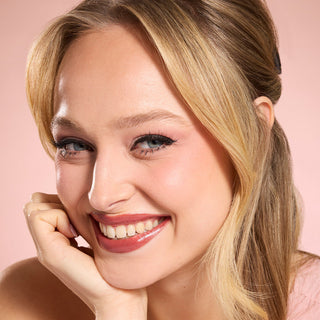 Woman with blonde hair and pink lipstick smiling against a pink background