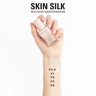 Revolution Skin Silk serum foundation bottle held by a hand with swatches on an arm.