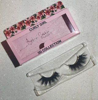 False eyelashes in a clear case with a pink box labeled 'Curly Girl' on a gray surface.
