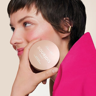 Woman holding a Bourjois compact mirror with a pink background
