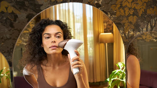 Woman holding a white handheld device in front of a decorative mirror.