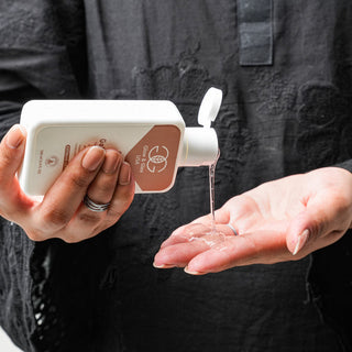 Person pouring liquid soap from a dispenser into their hand against a dark background