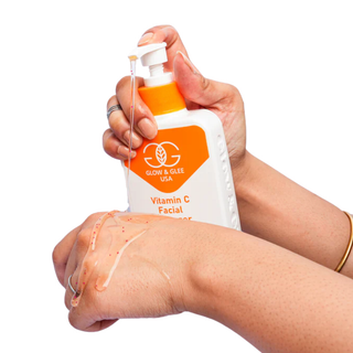 Hand holding a bottle of Glow & Glee USA Vitamin C Facial Serum with a white background