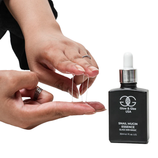 Person holding a dropper with snail mucin essence next to a bottle of Glow & Gleam USA snail mucin essence.